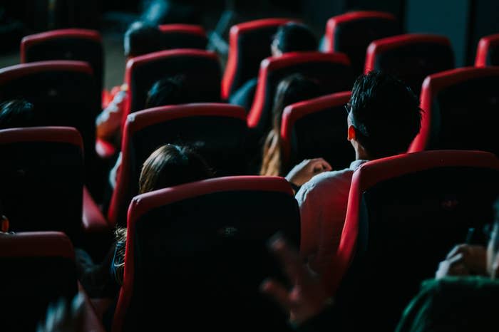 People sitting in a movie theater, viewed from behind. Chairs are visible