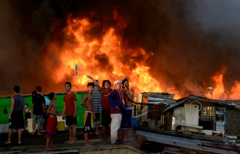 Residents wave to a helicopter that uses a water bucket to help douse fire that swept through a crowded Manila shanty town on November 25, 2015