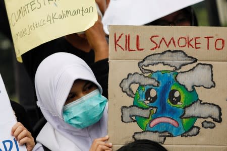 A girl holds a sign as she takes part on a Global Climate Strike rally as smog covers the city due to the forest fires in Palangka Raya