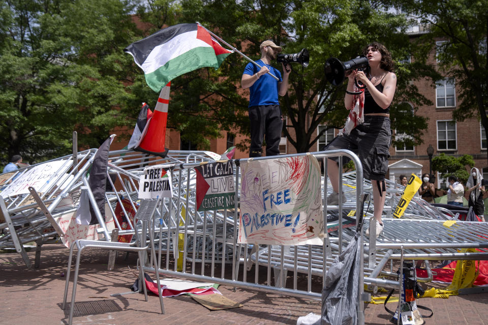 FILE - People stand atop a pile of barricades as they lead a chant at an encampment by students protesting against the Israel-Hamas war at George Washington University, Tuesday, April 30, 2024, in Washington. (AP Photo/Mark Schiefelbein, File)