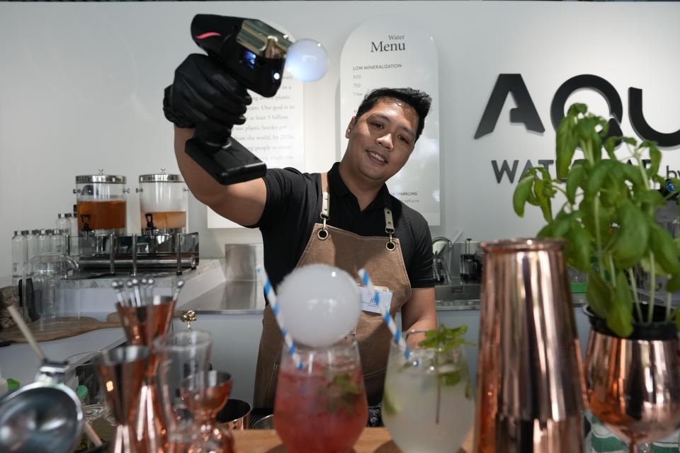 JC, mixologist, blows smoke bubbles atop a gourmet water cocktail he is preparing at the AQUA Water Bar by LUQEL in Dubai, United Arab Emirates, Tuesday, July 11, 2023. Dubai's gourmet water bar joins a growing list of unique businesses that have sprouted out of the uninterrupted stretches of windblown sand dunes turned into a bustling desert metropolis, complete with the world's tallest building, cavernous malls, and palm-shaped man-made islands. (AP Photo/Kamran Jebreili)