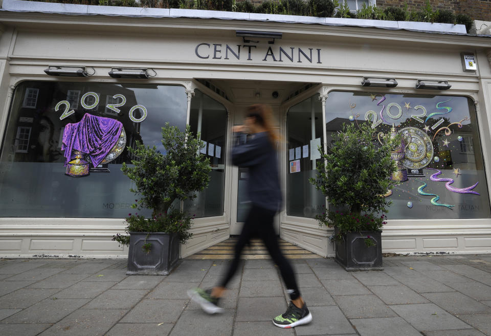A pedestrian passes signs on the window of a closed Italian restaurant showing the Wimbledon winners trophies in Wimbledon in London, Monday, June 29, 2020. The 2020 Wimbledon Tennis Championships, due to start Monday were cancelled due to the Coronavirus pandemic. (AP Photo/Kirsty Wigglesworth)