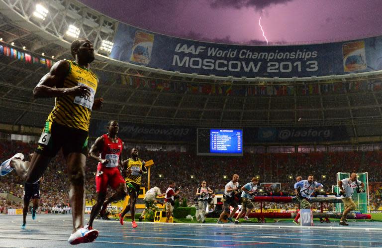 Jamaica's Usain Bolt (L) wins the 100 metres final at the 2013 IAAF World Championships at the Luzhniki stadium in Moscow on August 11, 2013 as lightning strikes in the background
