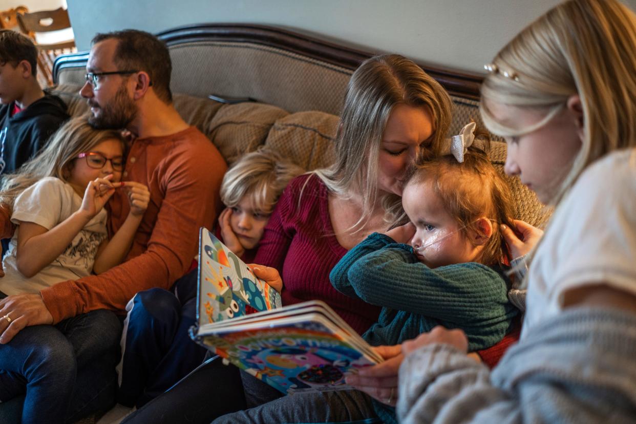 Jewel Calleja, of Livonia, kisses her daughter, CC Calleja, right, while sitting with (left to right), her son Colin Calleja, 11; daughter, Evelyn Calleja, 6; husband, Phil Calleja; son, Riley Calleja, 7, and daughter, Adelina Calleja, 9, in the living room of their home in Livonia on Dec. 22, 2023, while reading a book and watching television together. CC was born with Trisomy 18 and despite intense pressure to terminate the pregnancy, the Callejas say CC is now 4 years old and a valued and interactive member of the family.