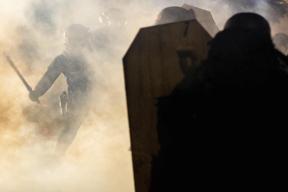 In this Aug. 16, 2020 photo, a Portland police officer wields a club against a protester amidst a cloud of teargas outside of the Penumbra Kelly building in Northeast Portland, Ore. Most police officers who violate citizens’ rights get away with it because the law is heavily stacked in their favor, legal experts say. (Maranie Rae Staab via AP)