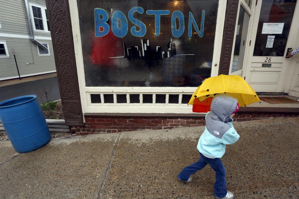 A child with an umbrella passes by a window painted with "Boston" near the Boston Marathon start line in Hopkinton