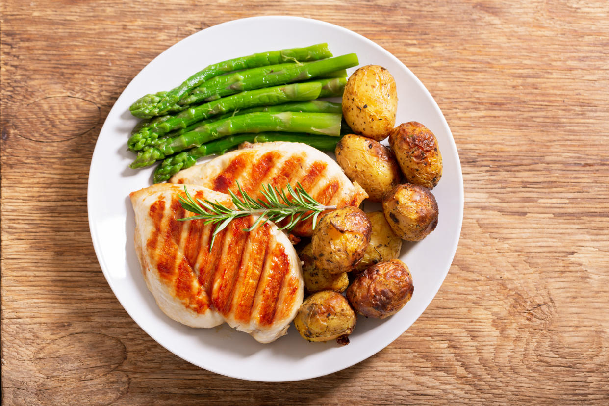 A plate containing two pork chops and side helpings of asparagus stalks and small potatoes.