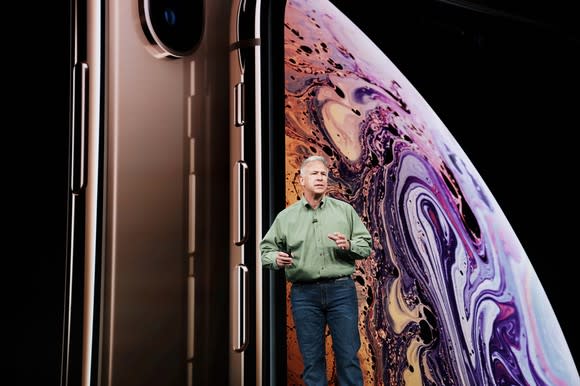 Apple exec Phil Schiller stands on a stage in front of giant renderings of an iPhone and an unspecified planet