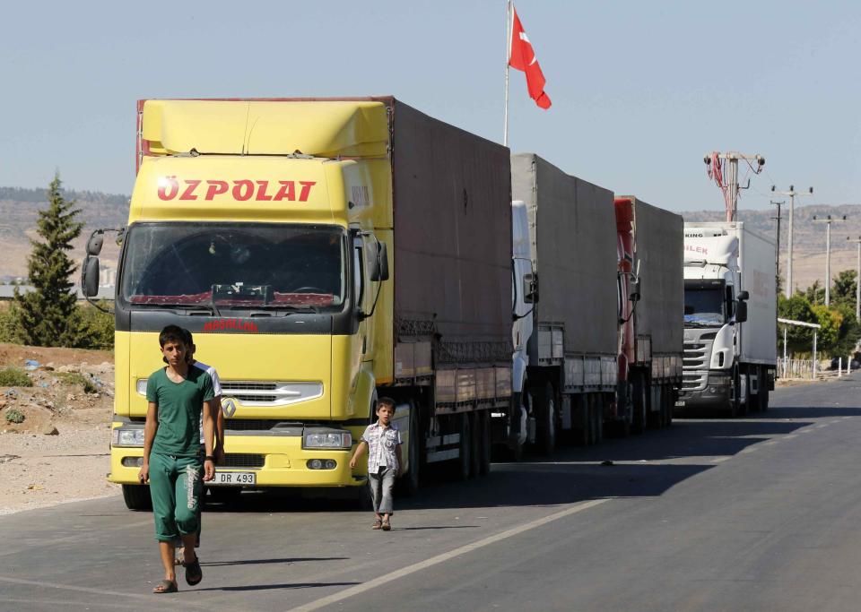 Locals walk past trucks lined up at the Oncupinar border crossing on the Turkish-Syrian border in the southeastern city of Kilis September 5, 2013. Every day, hundreds of trucks piled high with goods ranging from cooking oil to cement and nappies form queues stretching for miles at Oncupinar, now a bustling hub for trade with Syria. REUTERS/Umit Bektas (TURKEY - Tags: POLITICS BUSINESS CIVIL UNREST CONFLICT)