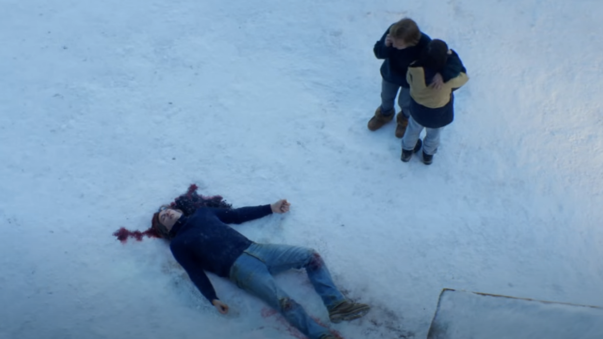  Still from Anatomy of a Fall showing two people looking on in horror at a dead man on a snowy floor. 
