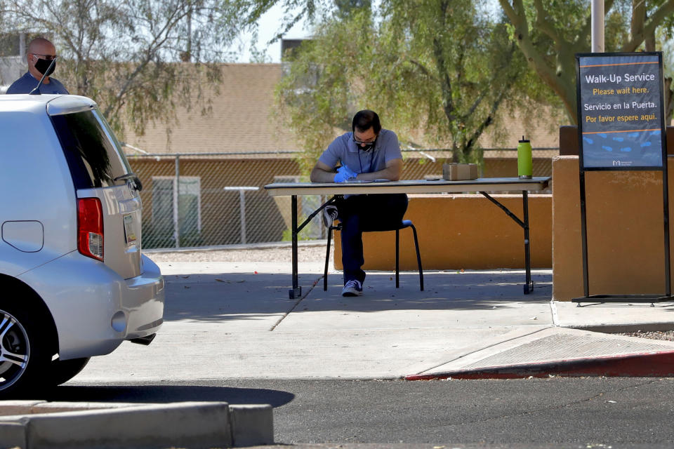 In this Thursday, June 18, 2020, photo, a man waits to check out books curbside from the Guadalupe library in Guadalupe, Ariz. As the coronavirus spreads deeper across America, it's ravaging through the homes and communities of Latinos from the suburbs of the nation's capital to the farm fields of Florida to the sprawling suburbs of Phoenix and countless communities in between. (AP Photo/Matt York)