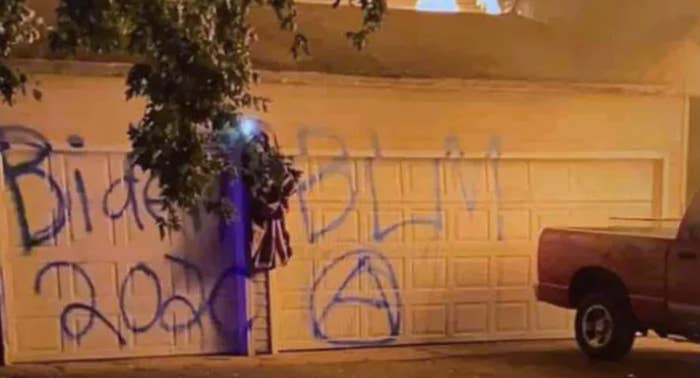 A garage is spray-painted with the messages "Biden 2020," "BLM," and an anarchy symbol