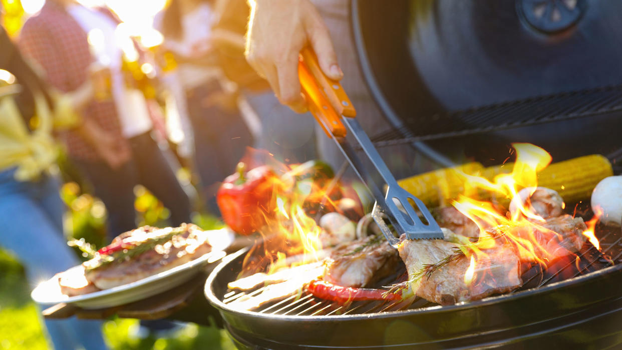  Food cooking on a grill with people socialising in background. 