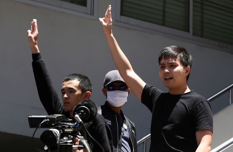 Pro-democracy leaders Tattep Ruangprapaikitseree and Panumas Singprom, flash the three-fingers salute as they are escorted by police officers after being arrested, at a police station in Bangkok