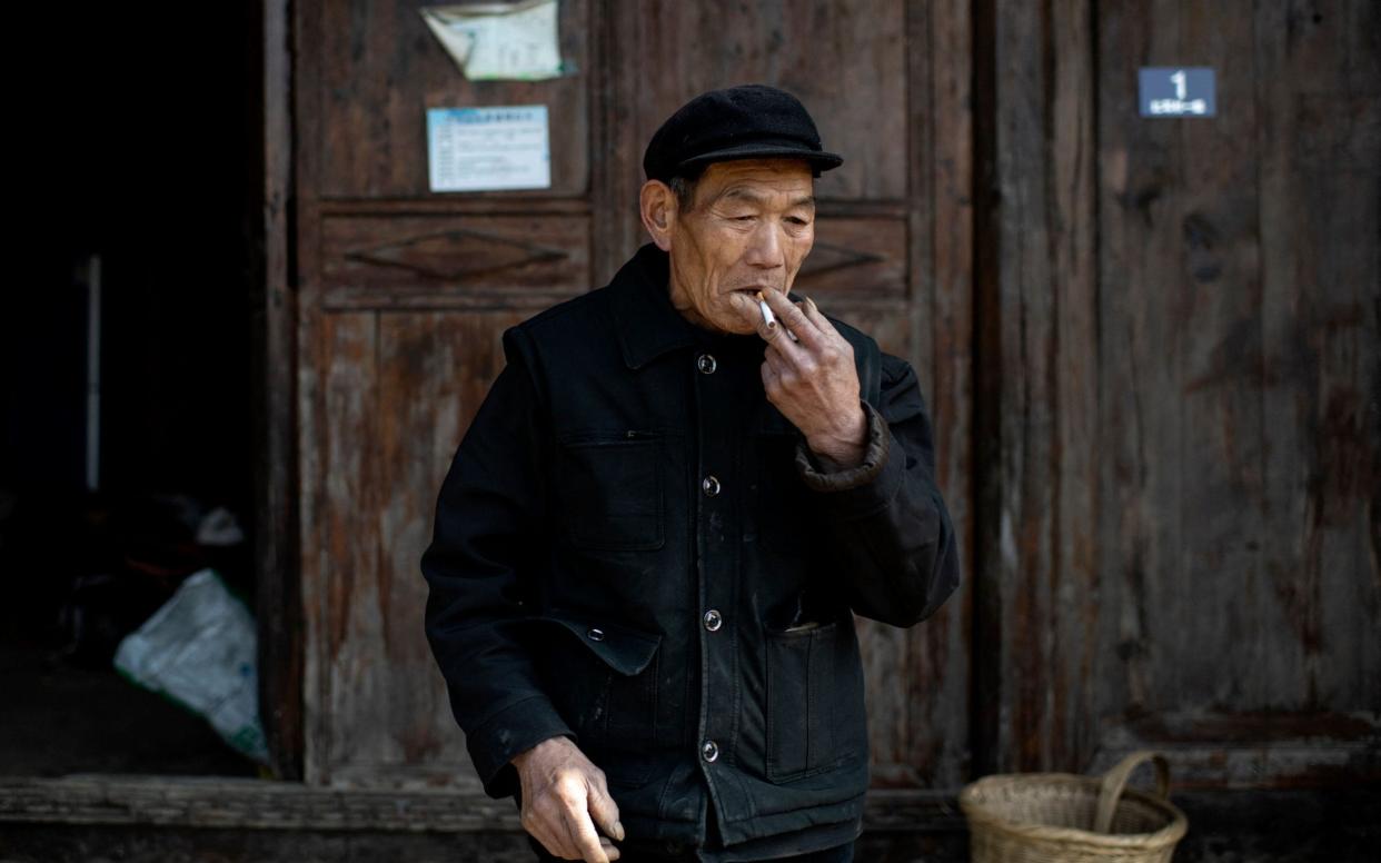 This picture taken on January 13, 2021 shows farmer Mi Jiazhi smoking in front of his old residence in Baojing county, in central China's Hunan province. - China's decades-long war to eradicate extreme poverty has yielded remarkable results, with Chinese President Xi Jinping declaring the target was reached in 2020 heralding a "major victory". But reality on the ground is patchier, with experts warning that rising incomes have made China's poverty line outdated. - Noel Celis/AFP