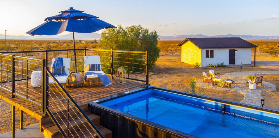 Small wooden deck with two lounge chairs and an umbrella sits level with the ModPools shipping container pool.