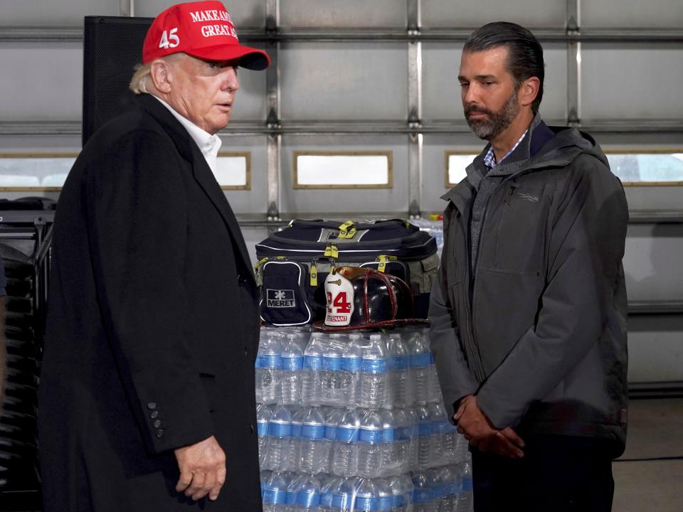 Donald Trump and Donald Trump Jr. stand in front of a pallet of water bottles.
