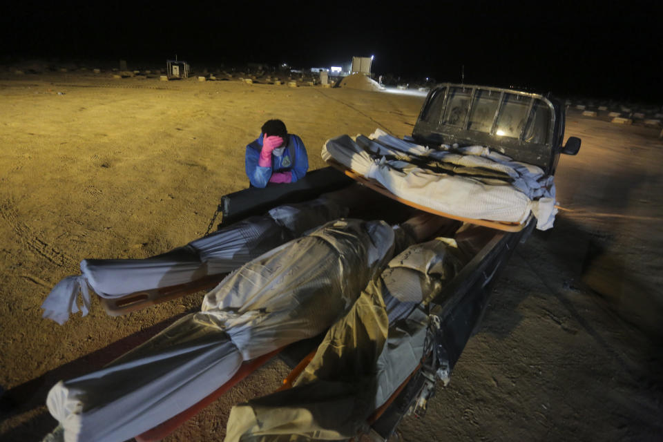 A member of the Shiite Imam Ali brigades militia stands next to bodies of coronavirus victims during a funeral at Wadi al-Salam cemetery near Najaf, Iraq, Monday, July 20, 2020. A special burial ground near the Wadi al-Salam cemetery has been created specifically for COVID-19 victims since rejections of such burials have continued in Baghdad cemeteries and elsewhere in Iraq. (AP Photo/Anmar Khalil)