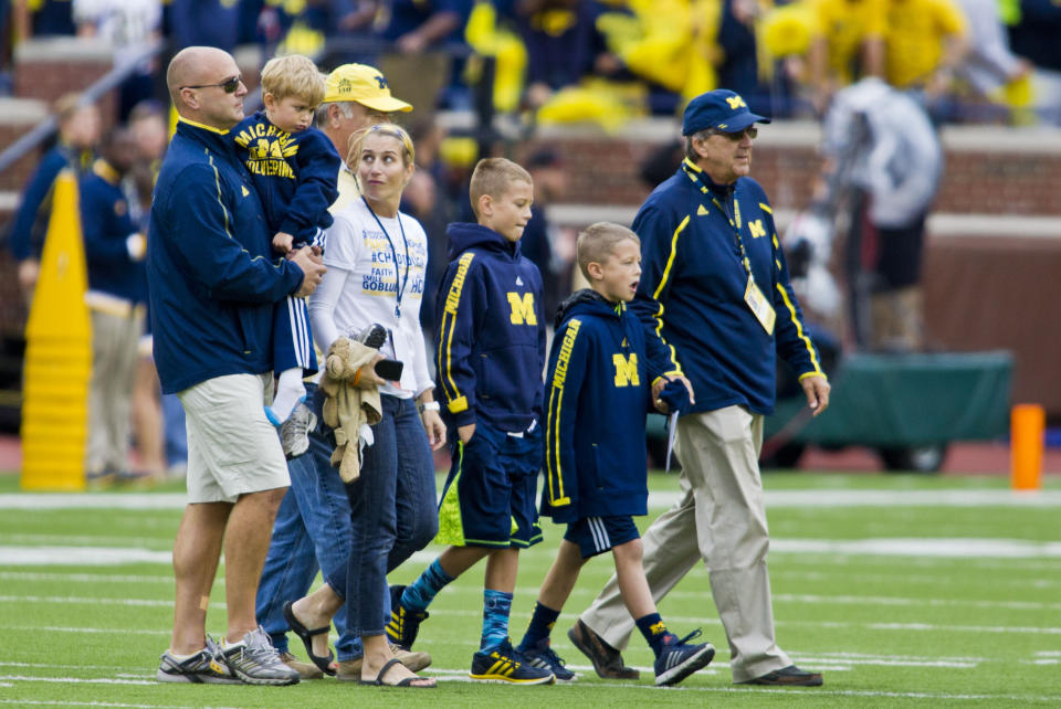 FILE - Former Michigan coach Lloyd Carr, far right, leads his grandsons CJ and Tommy Carr, daughter-in-law Tammi Carr, and son Jason Carr, left, holding his son Chad, onto the Michigan Stadium field for the coin toss before an NCAA college football game against Oregon State in Ann Arbor, Mich., Sept. 12, 2015. CJ will be among the hundreds of football players to sign a national letter of intent this week, sealing his commitment to join Notre Dame, but no one has a story quite the same. (AP Photo/Tony Ding, File)