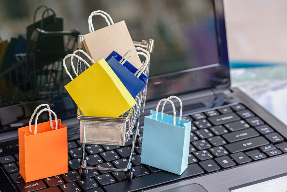 Five paper shopping bags and a shopping cart on a laptop keyboard. Concept about online shopping that customers can buy everything from home or office and the messenger will deliver to the doorstep.