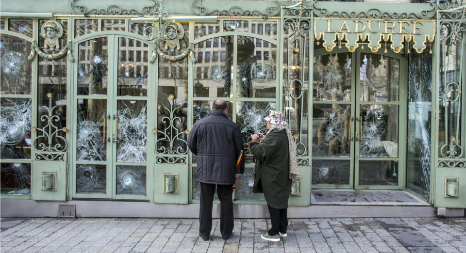 Bystanders take snapshots of the smashed windows of the famed tea salon Laduree on the Champs Elysees the day after it was vandalized during the 18th straight weekend of demonstrations by the yellow vests, in Paris, France, Sunday, March 17, 2019. Paris cleaned up one of the world's most glamorous avenues Saturday after resurgent rioting by yellow vest protesters angry at President Emmanuel Macron stunned the nation. (AP Photo/Rafael Yaghobzadeh)