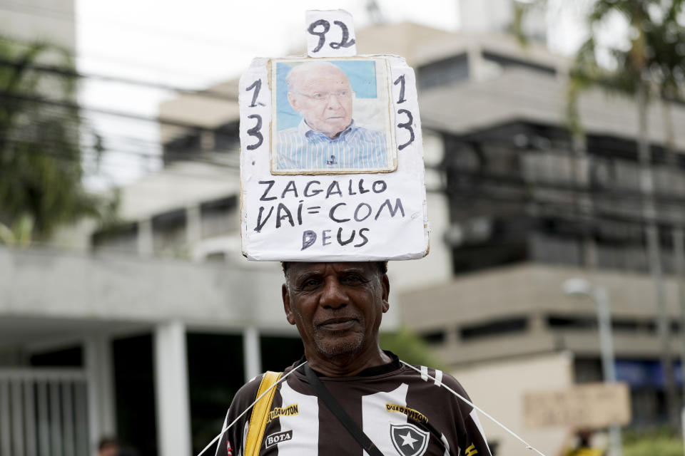 A mourner stands with a banner reading in Portuguese, "Zagallo, go with God" referring to former Brazilian soccer coach and player Mario Zagallo, before his funeral service outside the Brazilian Football Confederation headquarters in Rio de Janeiro, Brazil, Sunday, Jan. 7, 2024. Zagallo, who reached the World Cup final a record five times, winning four, as a player and then a coach with Brazil, died at the age of 92. (AP Photo/Bruna Prado)