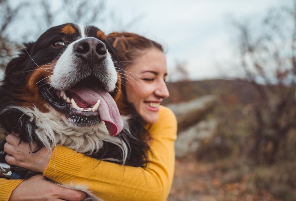 A person smiles while hugging a dog outdoors.