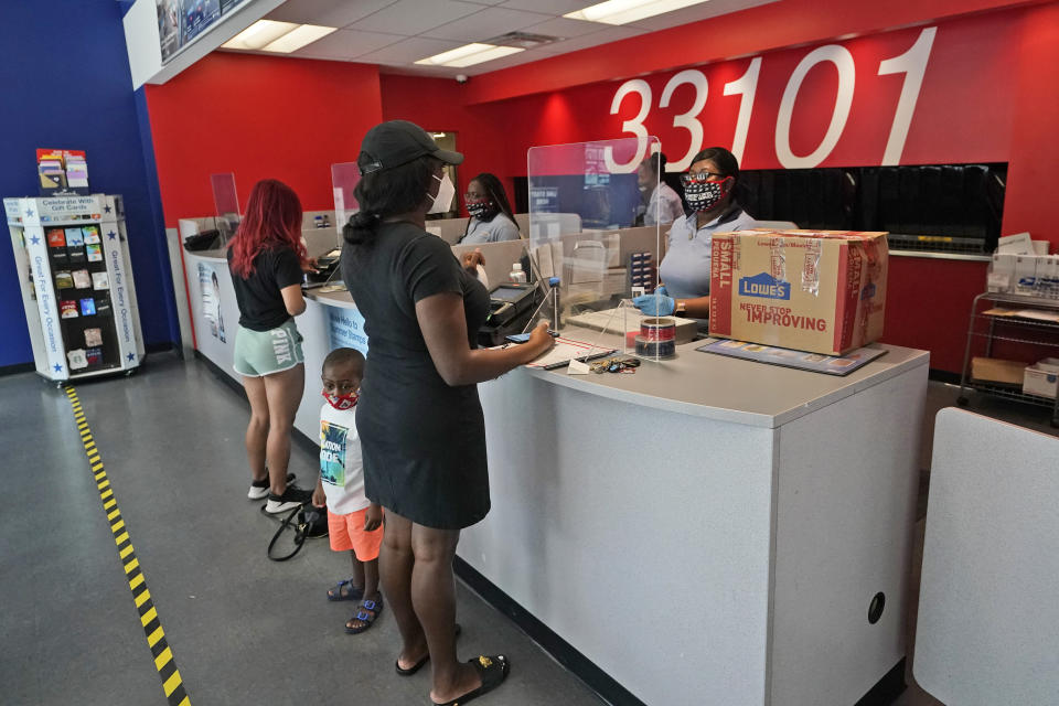 Postal workers attend customers at the Flagler Station post office, Tuesday, Aug. 25, 2020, in Miami. The pandemic has pushed the Postal Service into a central role in the 2020 elections, with tens of millions of people expected to vote by mail rather than in-person. At the same time, Trump has acknowledged he is withholding emergency aid from the service to make it harder to process mail-in ballots, as his election campaign legally challenges mail voting procedures in key states. (AP Photo/Wilfredo Lee)