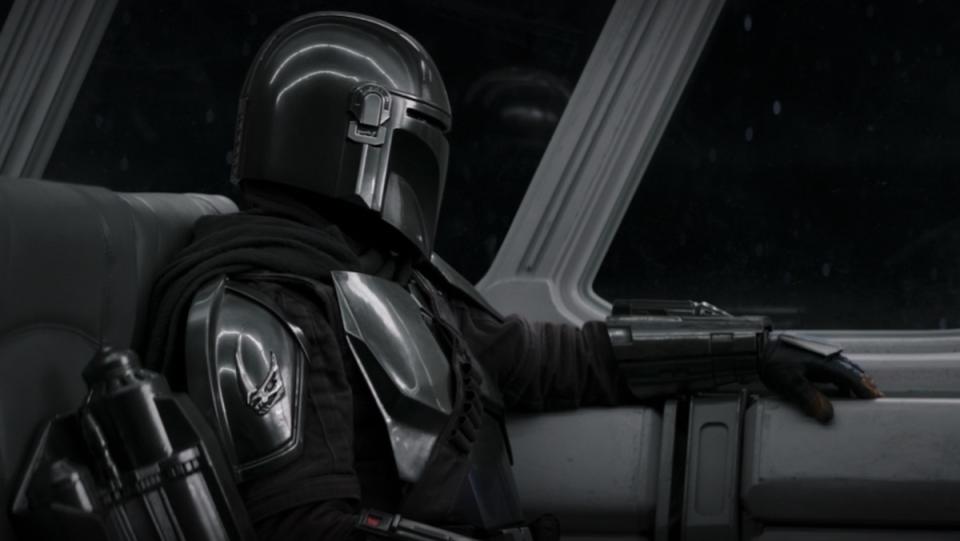The Mandalorian's Din Djarin sits alone looking out the window of a commercial ship on The Book of Boba Fett