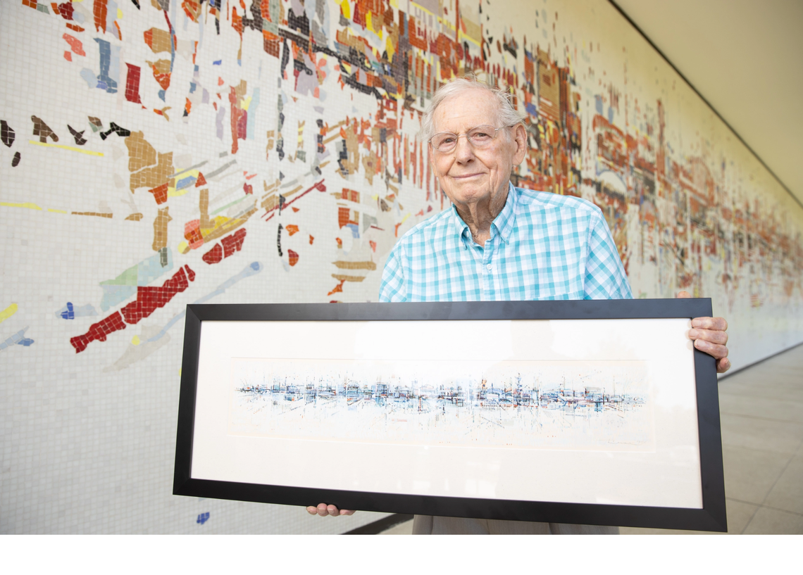 Artist Wayne Thiebaud, who died in 2021, holds a framed picture of “Water City” in front of the actual mural at the old SMUD headquarters building in East Sacramento.
