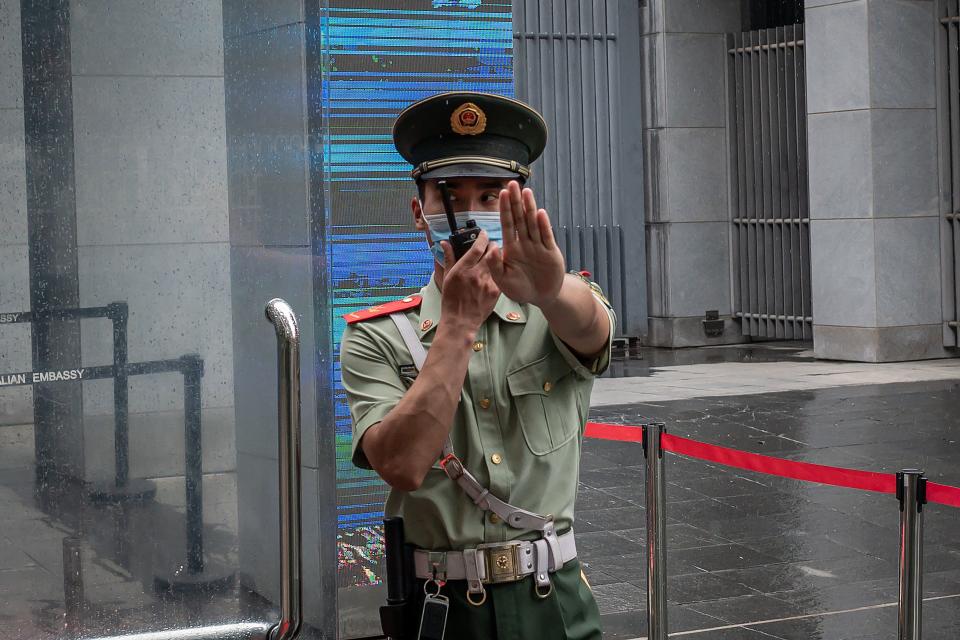 <p>FILE. A Chinese paramilitary police officer gestures and speaks over his two-way radio while standing at the entrance gate of the Australian embassy in Beijing on July 9, 2020. - China has suspended “indefinitely” its key economic dialogue with Australia.</p> (Photo by NICOLAS ASFOURI/AFP via Getty Images)