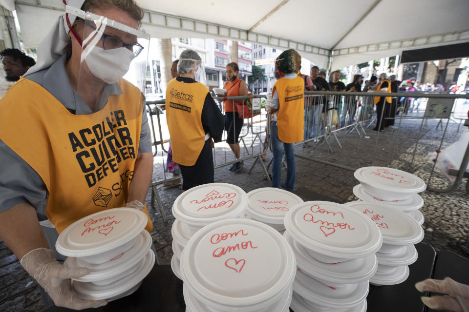 Volunteers from a Christian church serve food to homeless people, in containers covered with the Portuguese message: "With love," during a quarantine imposed by the state government to help contain the spread of the new coronavirus in Sao Paulo, Brazil, Monday, April 27, 2020. (AP Photo/Andre Penner)