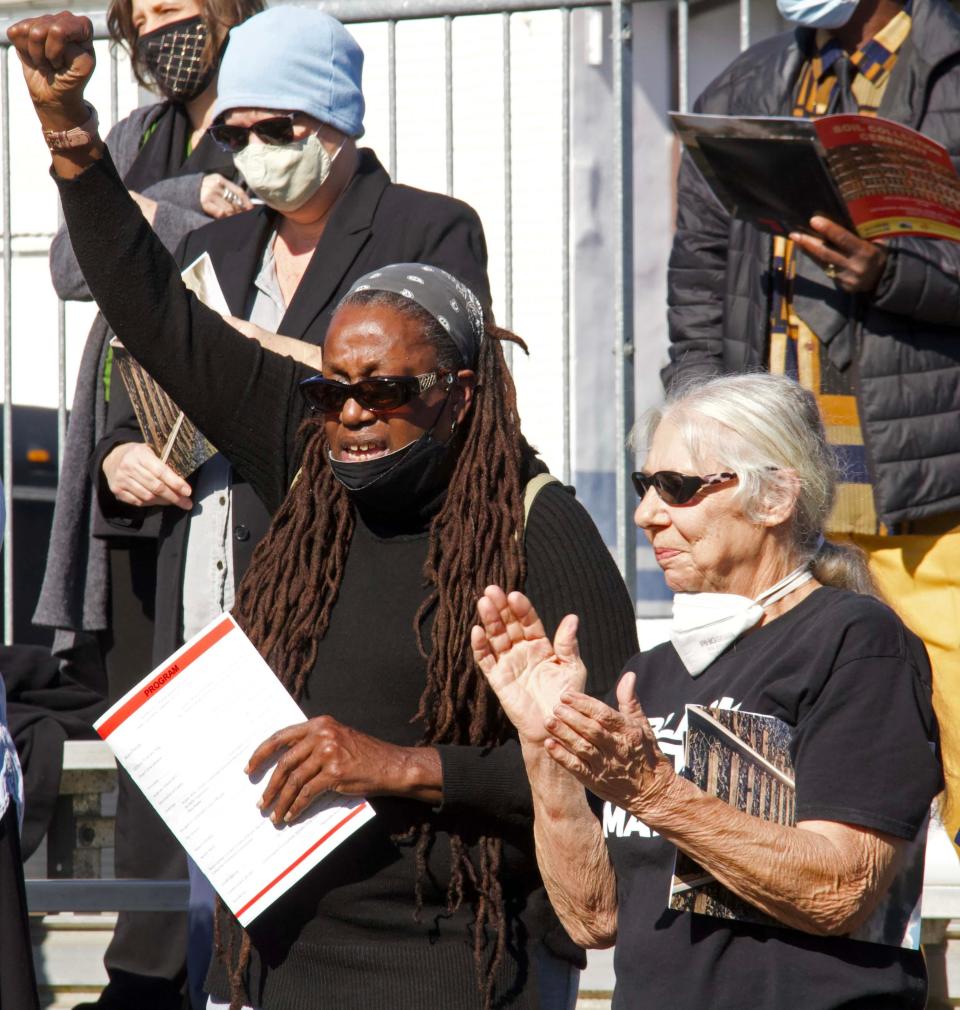 Nkwanda Jah (left) raises her fist in the air as Jackie Betz (right) claps at the Soil Collection Ceremony in Waldo held to memorialize lynching victims in the area. The two have been friends since 1986 according to Betz.