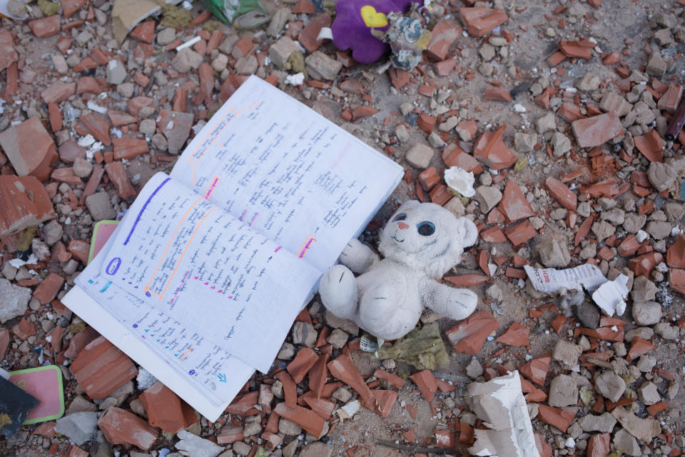 A toy and a notebook lie among crumbled bricks and other debris.