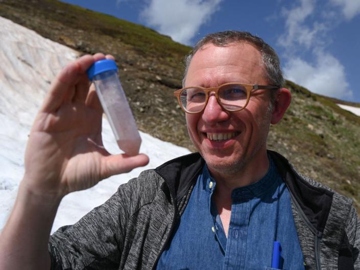 eric marechal smiling in the mountains holding up a sample tube of pink snow