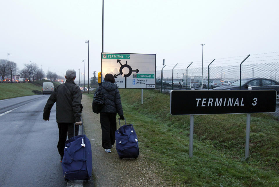 People walk along the side of the road to the airport terminal as taxi drivers stop the traffic on the highway leading to Paris, Thursday, Jan. 10, 2013 at Roissy airport. Taxi drivers across France were putting on the brakes to clog traffic, slow access to airports and force would-be passengers to find alternate transport in a strike over government efforts to deregulate the transportation industry. (AP Photo/Remy de la Mauviniere)