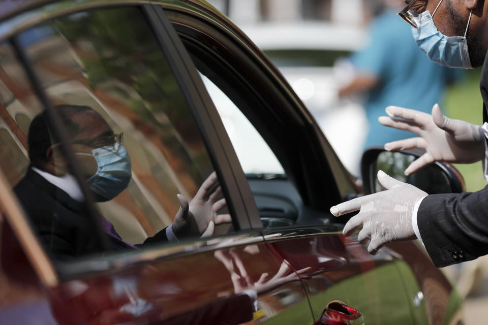 Rev. E.G. Shields, Jr., wears gloves and a protective face mask as he speaks through an open car window to a church representative picking up protective equipment for their congregation, Thursday, May 28, 2020, in Hanley Hills, Mo. Three groups representing black St. Louis-area clergy are combining forces to distribute about 150,000 masks to churches that plan to open as early as next week as restrictions surrounding the coronavirus outbreak ease. (AP Photo/Jeff Roberson)