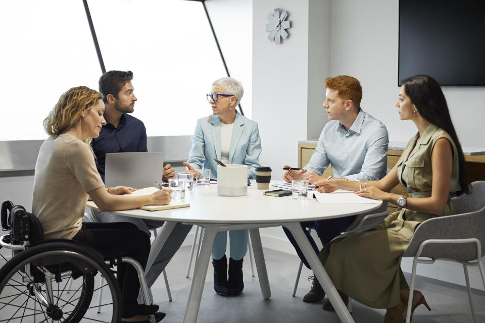 Male and female colleagues planning strategy in meeting. Business professionals discussing around conference table. They are in board room at office.