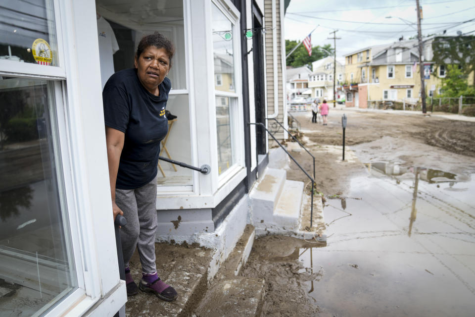 Kathy Eason, a worker at the Center for Highland Falls, stands on the storefront's stoop where she had been trapped by floodwaters the previous day, Monday, July 10, 2023, in Highland Falls, N.Y. Heavy rain has washed out roads and forced evacuations in the Northeast as more downpours were forecast throughout the day. One person in New York's Hudson Valley has drowned as she was trying to leave her home. (AP Photo/John Minchillo)