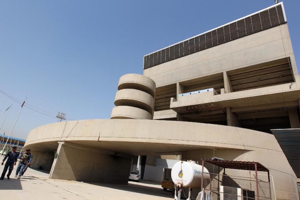 Iraqi security guards walk past the back side of the Le Corbusier-designed gymnasium of Baghad