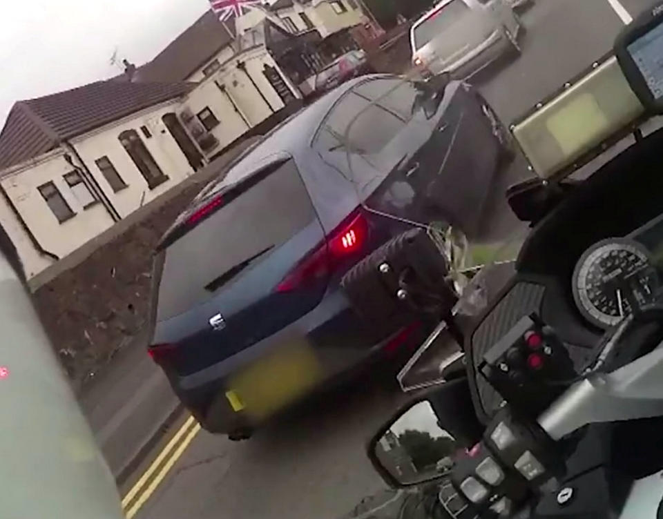 A teenage yob is facing jail after shocking footage caught him ramming a police officer off his motorbike in a stolen car. Callum Fellows, 18, was behind the wheel of a dark blue Seat Leon which was being followed by PC Steve Lovering. When the car stopped at traffic lights the officer drove up to the driver's door but Fellows suddenly reversed before steering straight into PC Lovering's BMW bike. CCTV and the officer’s body-cam captured the shocking moment when PC Lovering was sent sprawling onto Ashes Road in Oldbury, West Mids. The officer is heard shouting out in pain before radioing colleagues for help as Fellows sped away.