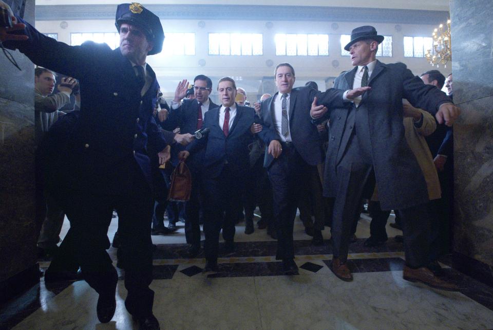 Jimmy Hoffa (Al Pacino, left) is led out of a media scrum by Bill Bufalino (Ray Romano) and Frank Sheeran (Robert De Niro) in 'The Irishman."