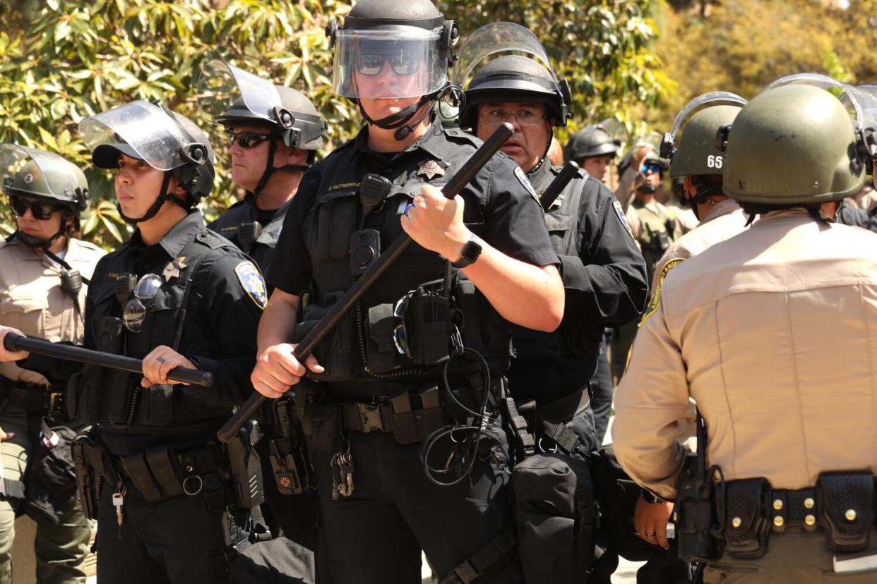 Uniformed officers in riot gear stand together.