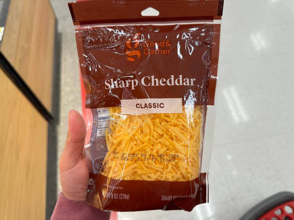 hand holding up a packet of shredded cheddar cheese at target