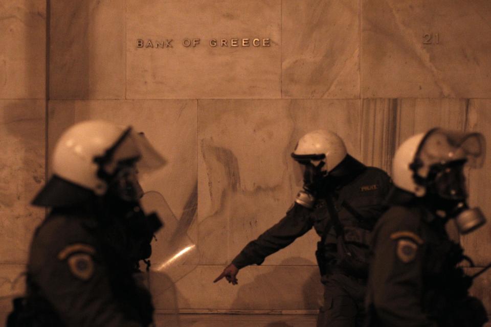 Riot policemen pass in front of the Bank of Greece during clashes with protesters in Athens, on Tuesday, April 1, 2014. Authorities banned all protests in a large section of central Athens for the Eurogroup and a later meeting of all European Union finance ministers. Nevertheless, some 7,500 anti-austerity demonstrators held three separate protests outside the exclusion zone, and some tried to break through a riot police cordon blocking their way to Parliament, where most marches in Athens wind up.(AP Photo/ Kostas Tsironis)