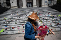 <p>A woman carries flowers to be placed with 215 pairs of children's shoes on the steps of the Vancouver Art Gallery as a memorial to the 215 children whose remains have been found buried at the site of a former residential school in Kamloops, in Vancouver, on Friday, May 28, 2021. Chief Rosanne Casimir of the Tk’emlups te Secwépemc First Nation First Nation said in a news release Thursday that the remains were confirmed last weekend with the help of a ground-penetrating radar specialist. THE CANADIAN PRESS/Darryl Dyck</p> 