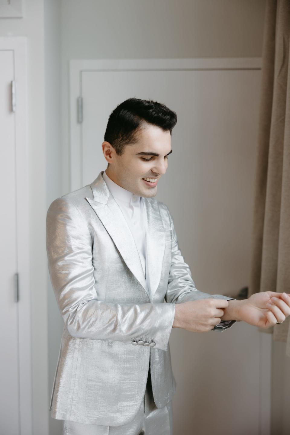 A man adjusts his silver suit.