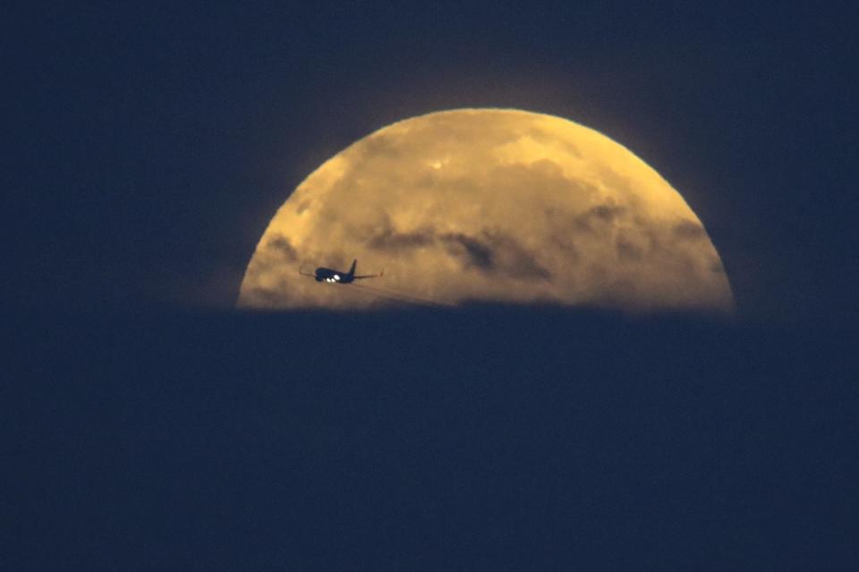 An airplane crosses in front of the full moon as it sets