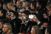 A man wearing a sanitary mask takes photos during the Dolce & Gabbana women's Fall Winter 2020-21 show, in Milan, Italy, Sunday, Feb. 23, 2020. After Giorgio Armani's last-minute decision to show his latest collection in an empty theater due to concerns about the new virus, the rest of Milan's runway shows scheduled for Sunday are to go ahead as planned, fashion officials confirmed. (AP Photo/Antonio Calanni)