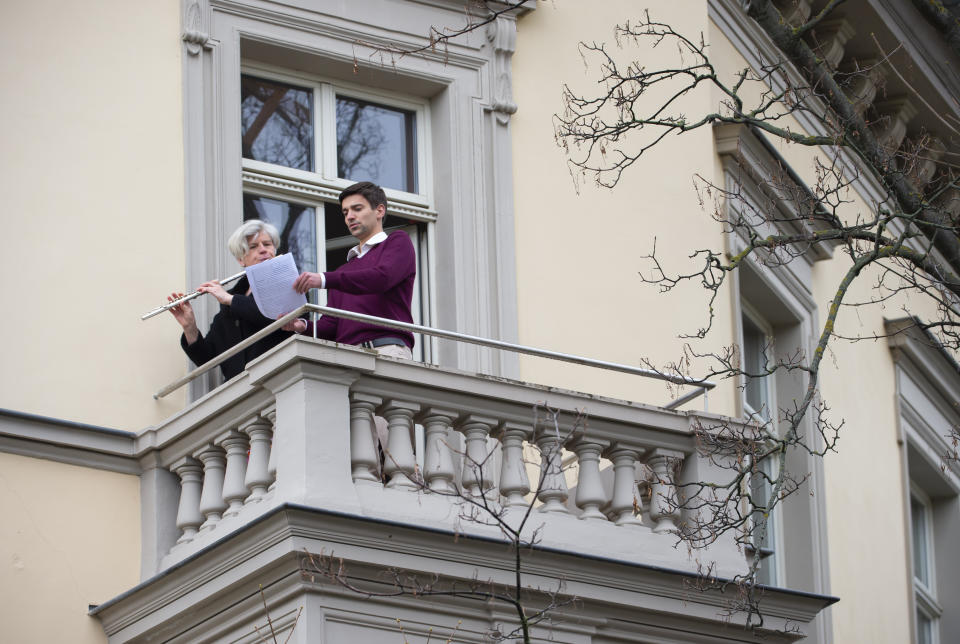 A flutist plays 'By loving forces silently surrounded...' by Dietrich Bonhoeffer on her balcony, as people practice social distancing due to coronavirus in Erfurt, central Germany, Sunday, March 29, 2020. For most people, the new coronavirus causes only mild or moderate symptoms, such as fever and cough. For some, especially older adults and people with existing health problems, it can cause more severe illness, including pneumonia. (AP Photo/Jens Meyer)